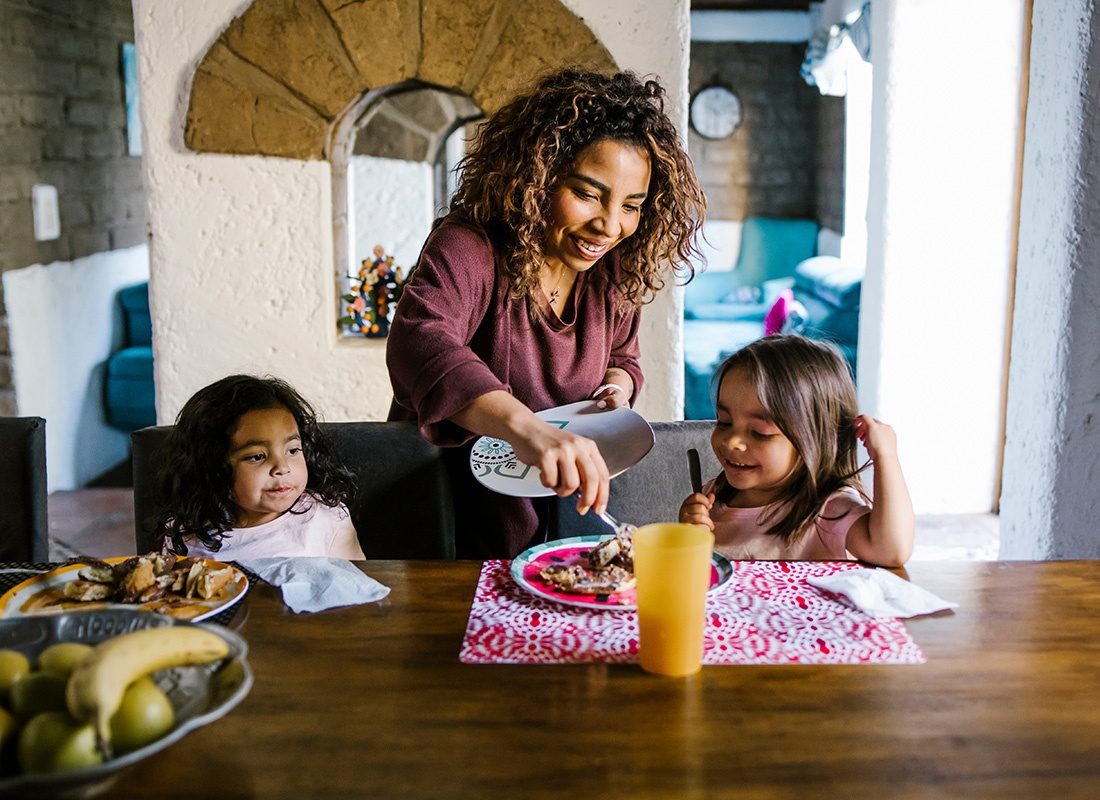 Contact - Smiling Young Mother Serving her Two Young Daughters Sitting at the Dining Table Breakfast in the Morning