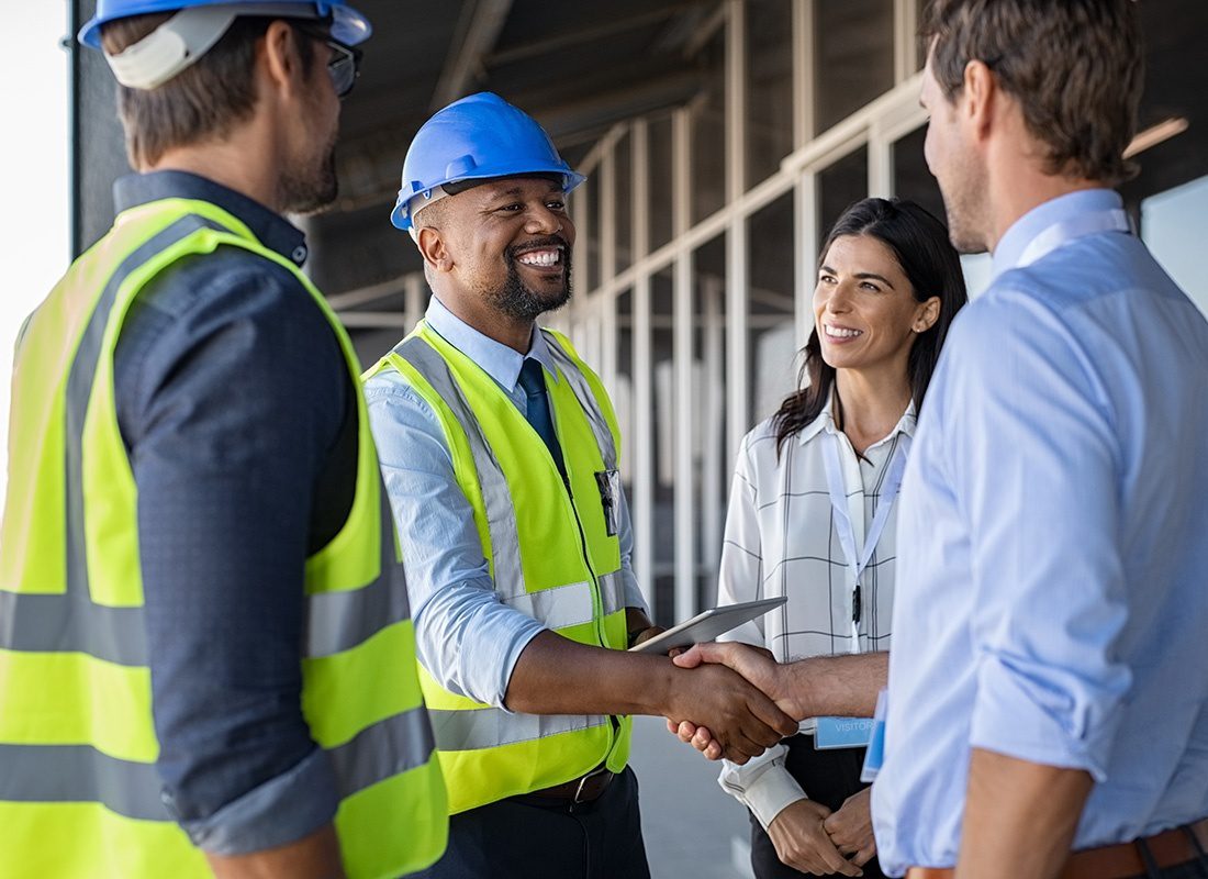 Insurance by Industry - Smiling Lead Contractor Holding a Tablet and Shaking Hands with a Team of Architects Outside a Commercial Building